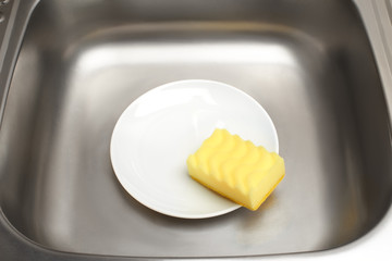 Kitchen sink with clean white plate and yellow cleaning sponge