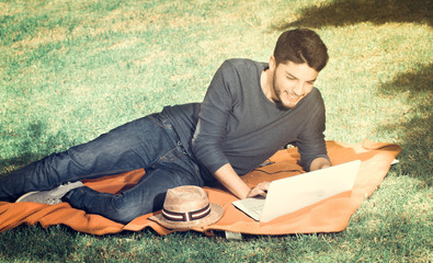 Handsome young man in the park sitting on the grass with a laptop, vintage effect