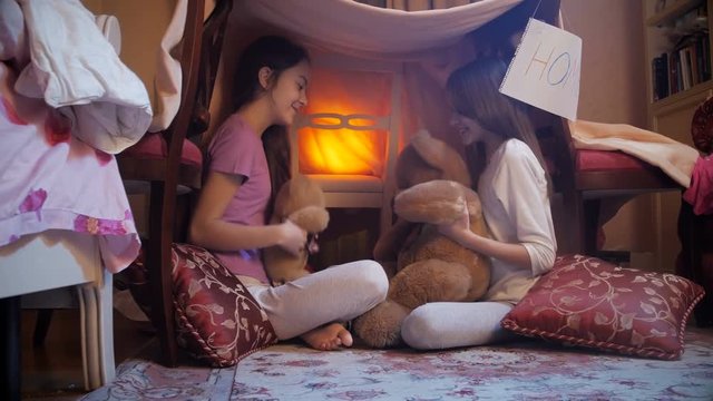 4k video of two girls in pajamas playing with teddy bear in selfmade tent at bedroom