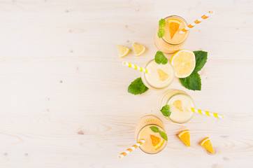 Freshly blended orange and yellow lemon smoothie in glass jars with straw, mint leaf,   slices orange and lemon, top view. White wooden board background, copy space.