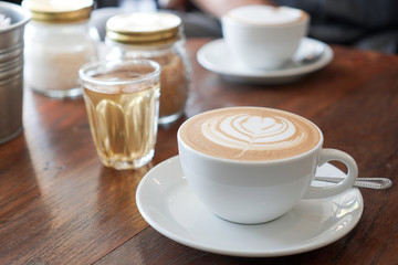 A cup of coffee with leaf pattern in a white cup on wooden background.