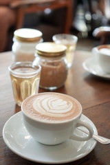A cup of coffee with leaf pattern in a white cup on wooden background.