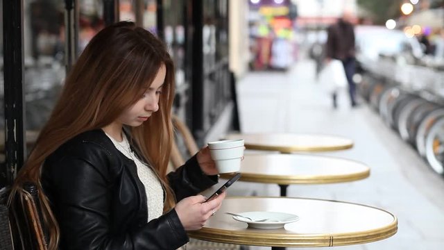 young girl checking emails and messages online on her phone in cafe in Paris