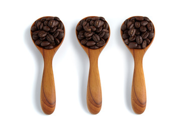 Three wooden spoon with coffee beans isolated on white background.