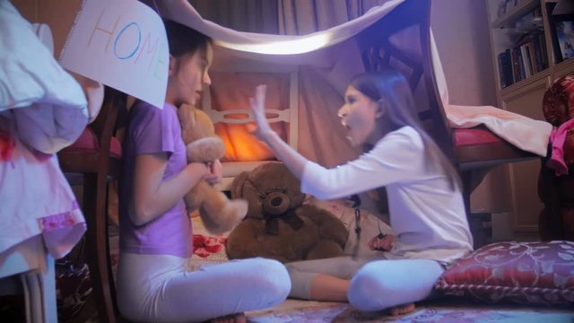 Two girls telling scary stories in tepee tent in bedroom at night