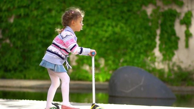 Young girl rides a scooter on a bike trail in the park.Children and childhood co