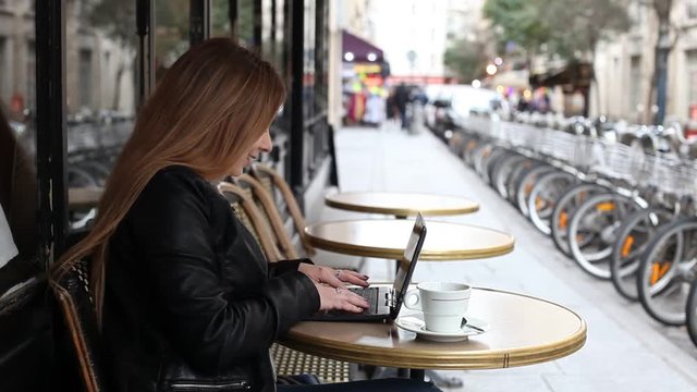 young woman using laptop computer in street cafe to check email