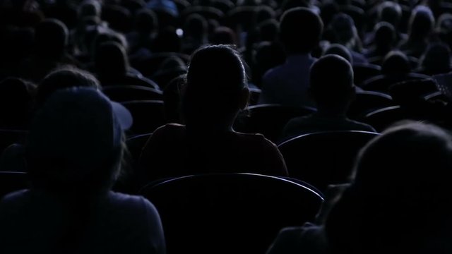The audience applauded for a performance or presentation in the theater. Video from the back. Children and adults alike
