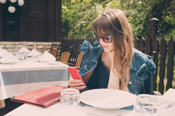 A smiling woman in a restaurant with phone in hands. waits to bring food