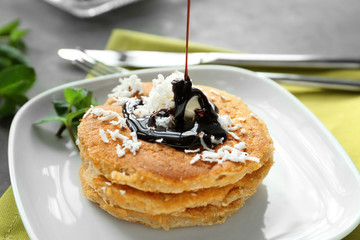 Pouring chocolate sauce onto tasty homemade coconut pancakes on plate