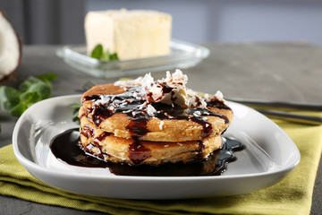 Tasty homemade coconut pancakes with chocolate sauce on plate