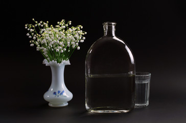 May-lily in a vase, a bottle and a glass of water