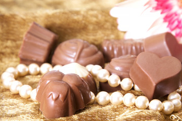 Assortment of chocolate bonbons and pearl necklace on golden background and flowers
