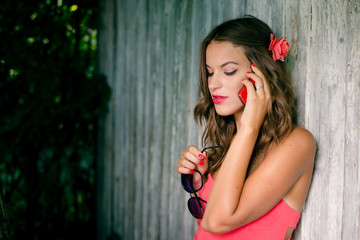 Young sexy stylish lady talking on mobile phone in front of wooden door on sunny summer day. Lifestyle portrait outdoor background