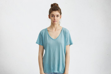 Portrait of pretty girl with hair bun biting lip, looking at camera with regretful or worried expression after she did something wrong. Frustrated young woman having confused indecisive look