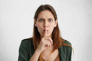 Annoyed brunette woman showing silence sign with her index finger. Pretty female with big dark eyes...