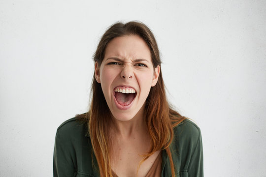 Close-up of irritated woman looking angrily in camera shouting having wide opened mouth being annoyed. Pretty woman wearing casual clothes having bad mood looking having rage and frowning expression