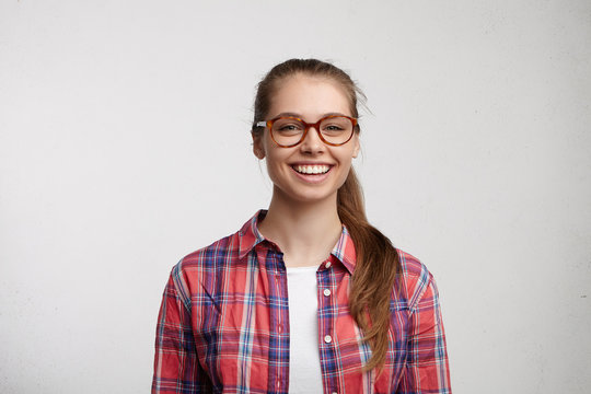 Cheerful woman with smooth cheeks and pleasant green eyes dressed casually wearing big elegant eyeglasses being pleased to hear good news. Portrait of happy woman posing over white background