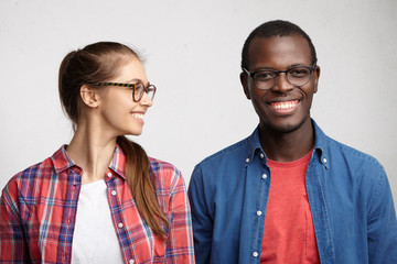Young mixed race couple: Woman with pony tail wearing eyeglasses and checked shirt looking with...