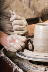 pottery, workshop, ceramics art concept - male master sculpt a utensil with sponge and carving tools, man hands work with potter's wheel, fingers form shape of raw clay, vertical