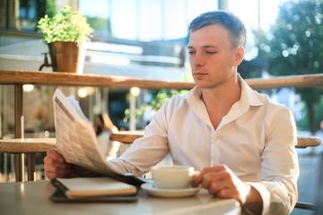 Man is reading a newspaper in a street cafe at lunch.