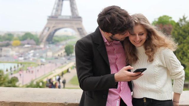 couple of tourists using smartphone and taking selfie photo near Eiffel tower in Paris, France