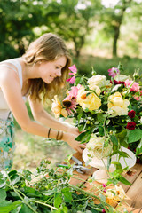 bouquet, people and floral arrangement concept - woman with beautiful bouquet of pink peonies, yellow and white roses, carnations and daisies, female florist at the table with flowers in garden