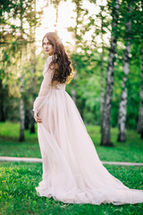 Obraz na płótnie Canvas beautiful young girl bride brunette in delicate Bridal boudoir gown of lace and tulle in beige color is outdoors, in a Park with trees, birches, profile