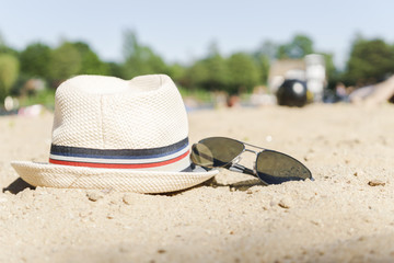 Hat and sunglasses on sand at the sity lake background.