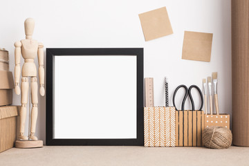 Black square picture frame mock up in styled modern artist workspace with brushes; scissors; dummy; sticky notes.
