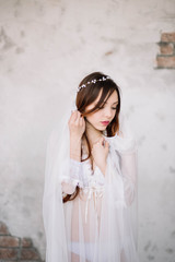 Bride's morning. Fine art wedding. Portrait of a young bride in white lace boudoir with wavy blonde hair and a bouquet in her hands posing looking down shyly