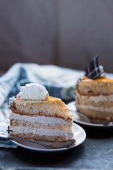 a beautiful delicious cake and the pieces in twoo white saucers beige yellow on cutting Board on dark black background close-up