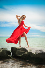 Beautiful woman in a bright red dress by the sea.