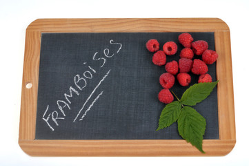 Framboises écrit sur une ardoise sur laquelle sont posées des framboises


