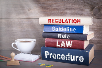 Regulation concept. Stack of books on wooden desk.
