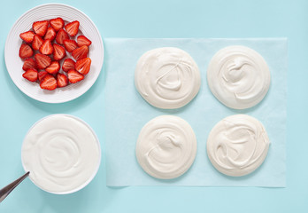 Meringue on a blue background with whipped cream and strawberries. Preparation of Pavlova cake. View from above.