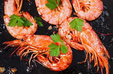 Grilled shrimps on black background. Delicious seafood appetizer served boiled or grilled with spices. Close up.