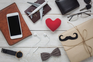 Top view Happy Father day with travel concept. Red heart shape on rustic wooden background. accessories with mustache,vintage bow tie,key,present,white mobile phone,earphone,watch and notebook. - Powered by Adobe