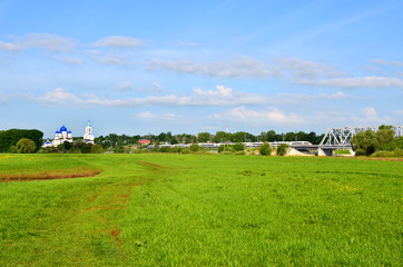Fototapeta na wymiar Bogolyubovo, spring landscape with a church, a green meadow and a high-speed train