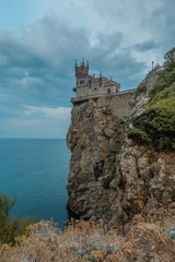 Fototapeta na wymiar The Swallow's nest (Lastochkino gnezdo) castle, Gaspra (Yalta), Crimea, Russia. A castle on the rock over the Black sea, a cloudy sky at the background, a trees and bushes on the rock.