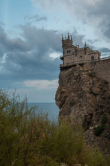 The Swallow's nest (Lastochkino gnezdo) castle, Gaspra (Yalta), Crimea, Russia. A castle on the rock over the Black sea, a cloudy sky at the background, a trees and bushes on the rock.