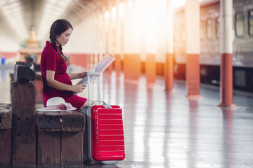 Asian pregnant woman holding map sitting on the wooden bench at railway station