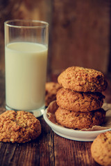 A close-up of a stack of pumpkin oat cookies on white parchment and gold swirl paper with golden raisins, cacao nibs and a glass of almond milk in the background.