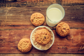 A close-up of a stack of pumpkin oat cookies on white parchment and gold swirl paper with golden raisins, cacao nibs and a glass of almond milk in the background.
