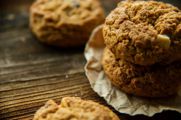 A close-up of a stack of pumpkin oat cookies on white parchment and gold swirl paper with golden raisins, cacao nibs and a glass of almond milk in the background.