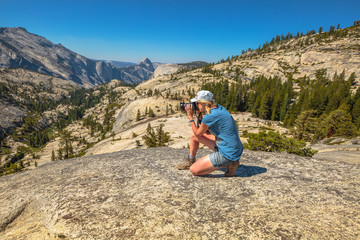 Naklejka premium Travel photographer takes shot of north side Half Dome on Olmsted Point. Tioga Road in Yosemite National Park, California, USA. Nature photographer taking pictures outdoors during hiking trip.