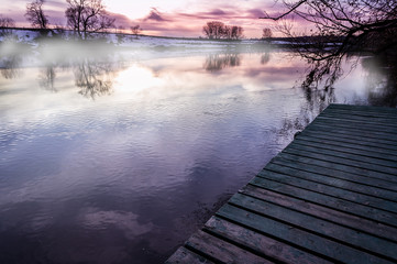 Wooden pier stretching into the river with fog at dawn