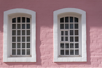Part of facade of old building with pink cracked brick walls and semi-circular windows.