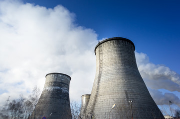 Two cooling towers emitting steam, with a blue sky background