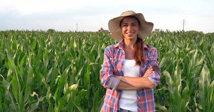 Beautiful girl (woman) farmer smiling, looking, checking corn fields, straw hat, greens background. Concept: ecology, corn, bio product, inspection, water, natural products, professional, environment.